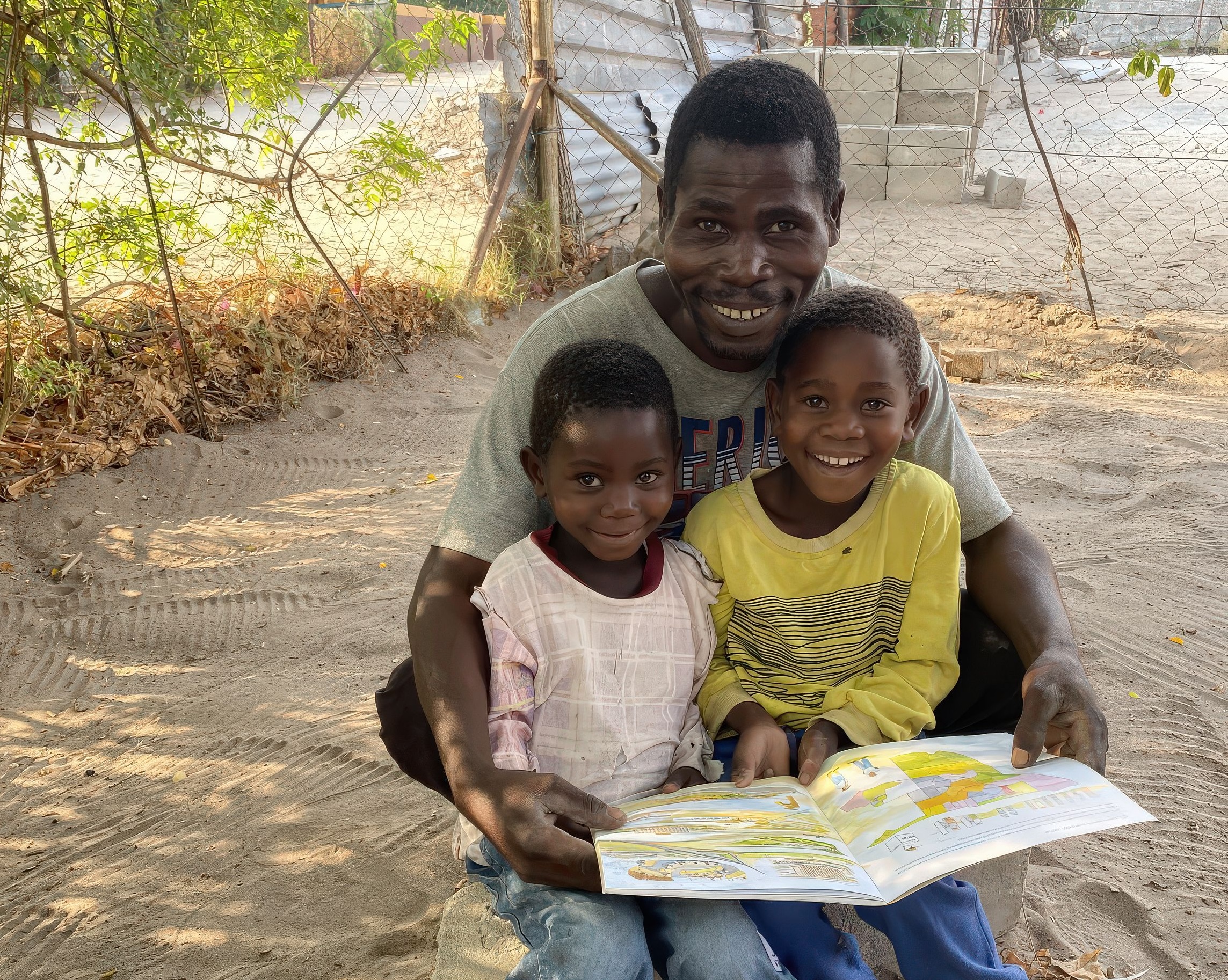 A man and his two children all smiling happily as they read the Children's Atlas of Namibia together.